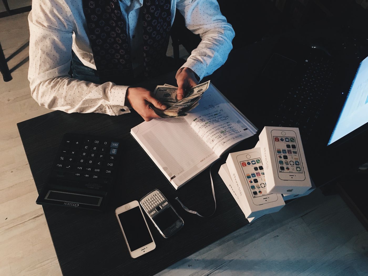 A flat-lay desk arrangement with a smartphone, a notebook and small electronic devices