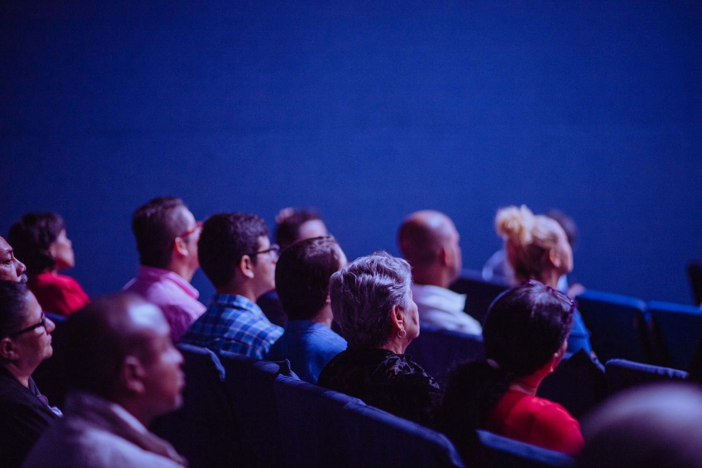 A crowd at an indoor event watching a speaker on a lit stage