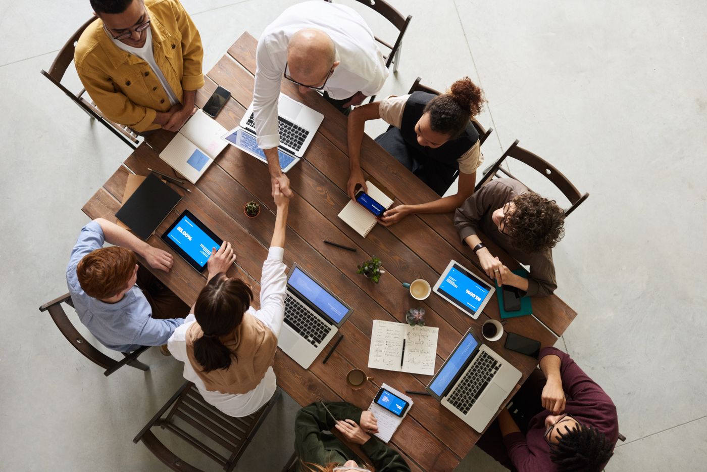 Four colleagues seated around a table in a bright open-plan office, working on laptops and talking