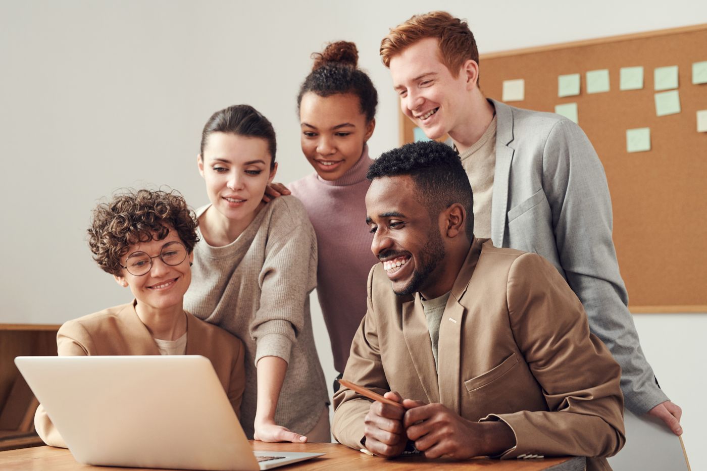 Five colleagues gathered around an open laptop in a bright office, looking at the screen together
